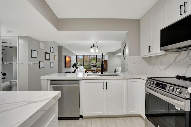 kitchen featuring appliances with stainless steel finishes, a sink, light stone countertops, white cabinetry, and backsplash