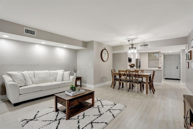 living room featuring light wood-type flooring, visible vents, and baseboards