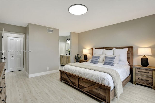 bedroom with ensuite bathroom, light wood-style flooring, visible vents, and baseboards