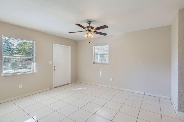 spare room featuring a ceiling fan, a wealth of natural light, and light tile patterned flooring