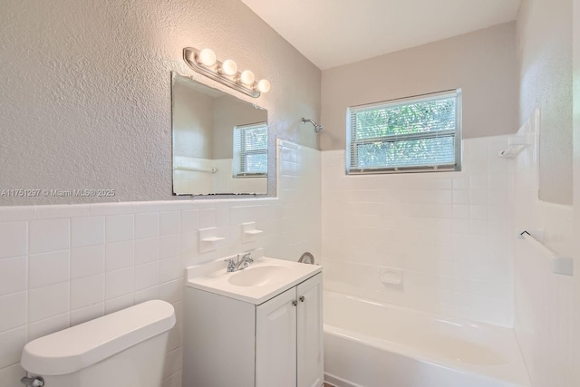 bathroom with a textured wall, toilet, shower / bath combination, vanity, and tile walls