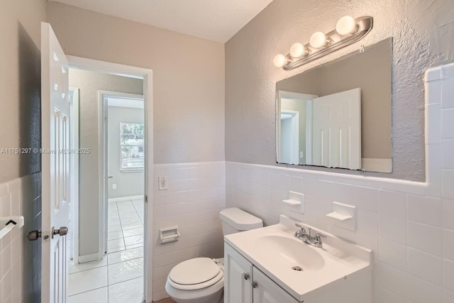 bathroom with a wainscoted wall, tile walls, toilet, vanity, and tile patterned flooring