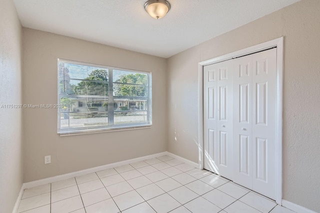 unfurnished bedroom featuring a closet, a textured ceiling, baseboards, and light tile patterned floors