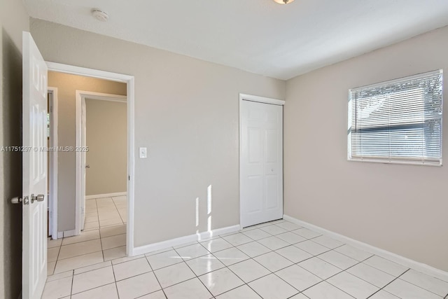 unfurnished bedroom featuring light tile patterned floors, baseboards, and a closet