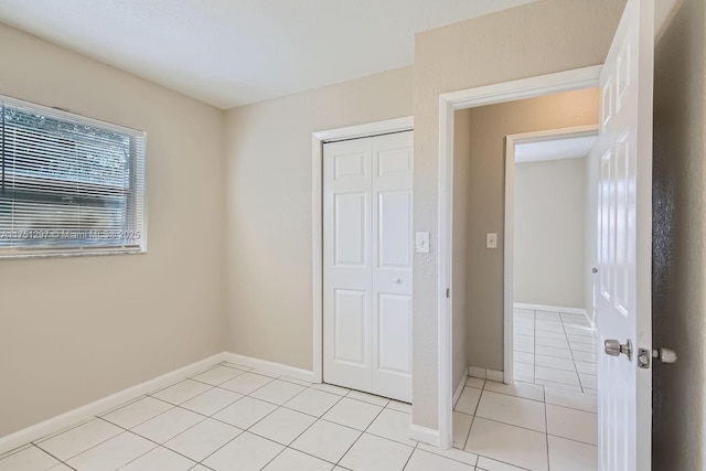 unfurnished bedroom featuring a closet, baseboards, and light tile patterned floors