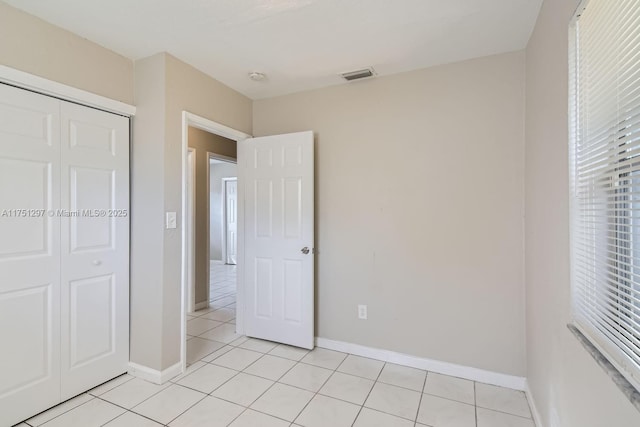 unfurnished bedroom featuring a closet, light tile patterned flooring, visible vents, and baseboards