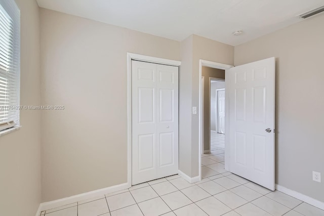 unfurnished bedroom featuring a closet, visible vents, baseboards, and light tile patterned floors