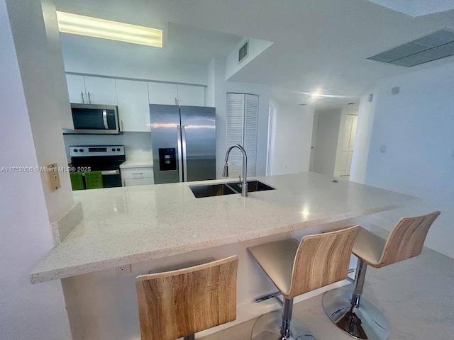 kitchen featuring a breakfast bar, visible vents, appliances with stainless steel finishes, white cabinetry, and a sink