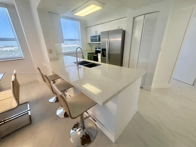 kitchen featuring white cabinets, appliances with stainless steel finishes, a breakfast bar, light stone countertops, and a sink