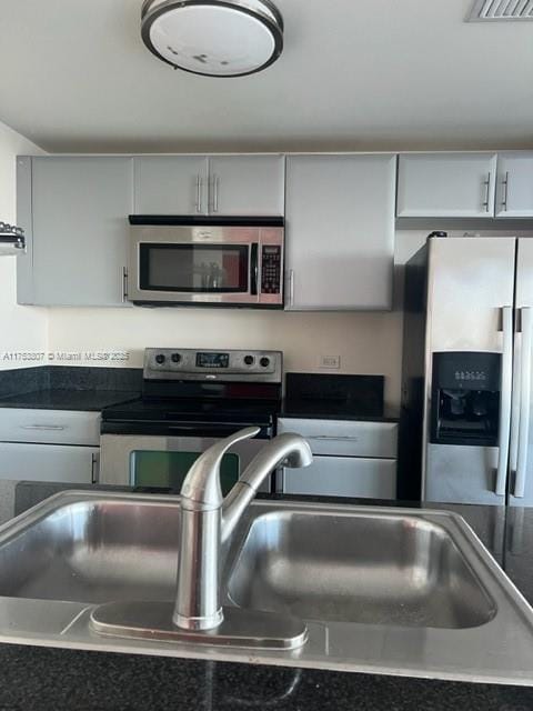 kitchen with a sink, stainless steel appliances, dark countertops, and gray cabinets