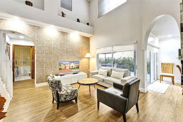 living room with arched walkways, a high ceiling, tile walls, baseboards, and light wood-type flooring