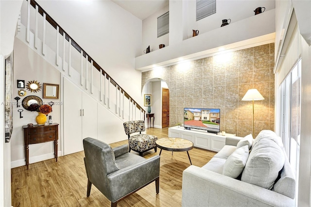 living area featuring light wood finished floors, baseboards, arched walkways, a high ceiling, and stairs