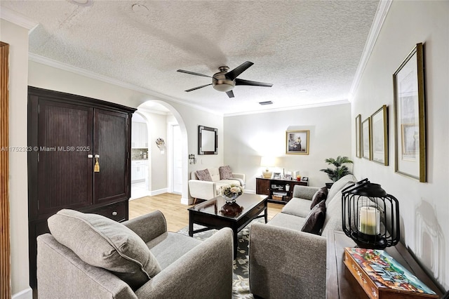 living area with arched walkways, ceiling fan, a textured ceiling, light wood-style floors, and crown molding