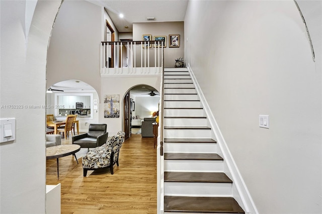 stairs with arched walkways, visible vents, a towering ceiling, a ceiling fan, and wood finished floors