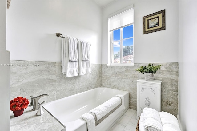 bathroom with marble finish floor, a wainscoted wall, and a bath