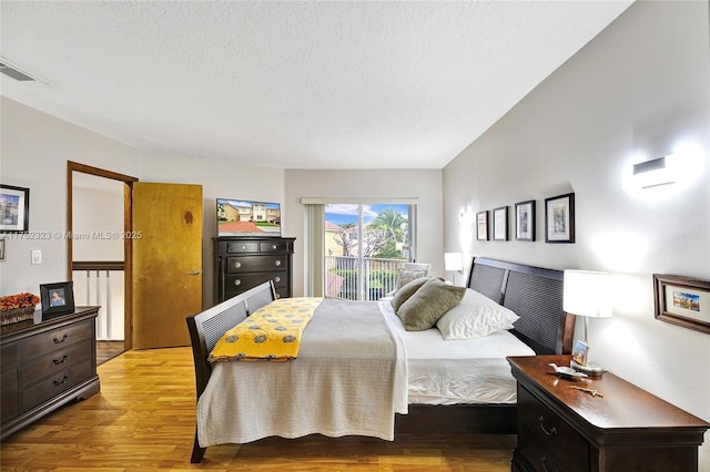 bedroom featuring access to exterior, visible vents, a textured ceiling, and wood finished floors