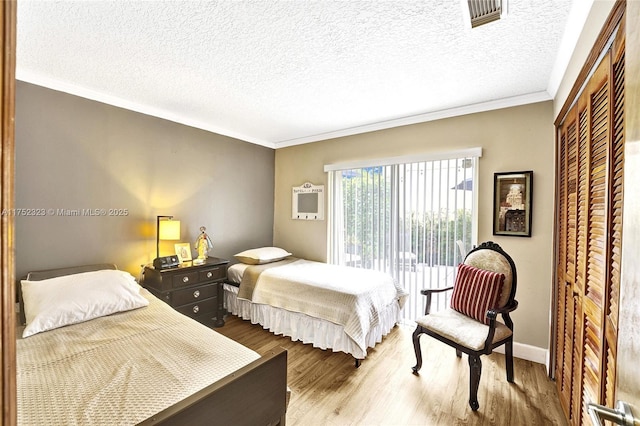 bedroom featuring a closet, visible vents, ornamental molding, a textured ceiling, and wood finished floors