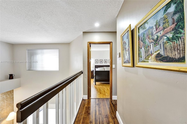 corridor with dark wood-style floors, baseboards, a textured ceiling, and an upstairs landing