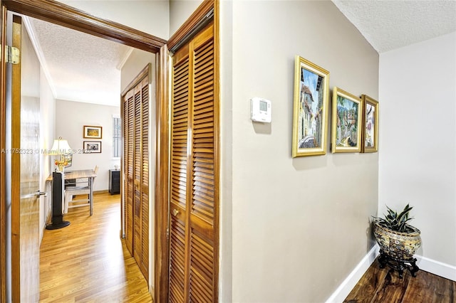 hallway with a textured ceiling, light wood finished floors, and baseboards