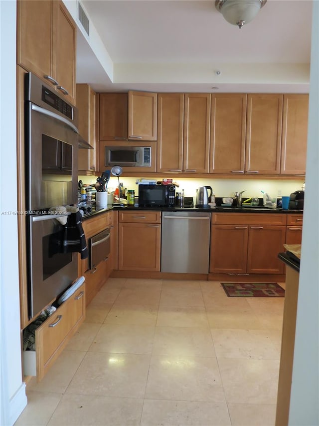 kitchen with a warming drawer, light tile patterned floors, stainless steel appliances, dark countertops, and a sink