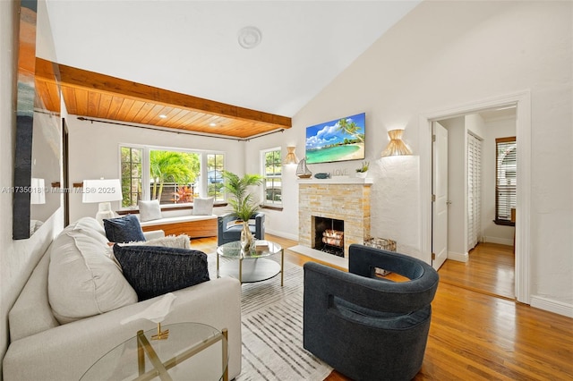 living area with beam ceiling, light wood finished floors, high vaulted ceiling, a lit fireplace, and baseboards