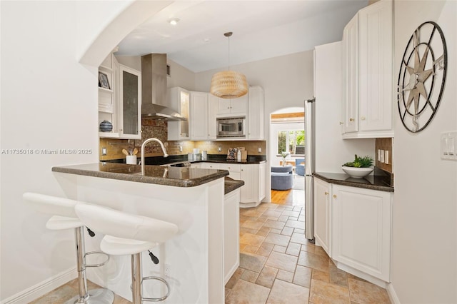 1109 NE 3rd St, Fort Lauderdale, FL 33301 - kitchen with white cabinetry, stainless steel microwave, backsplash, a peninsula, and wall chimney exhaust hood