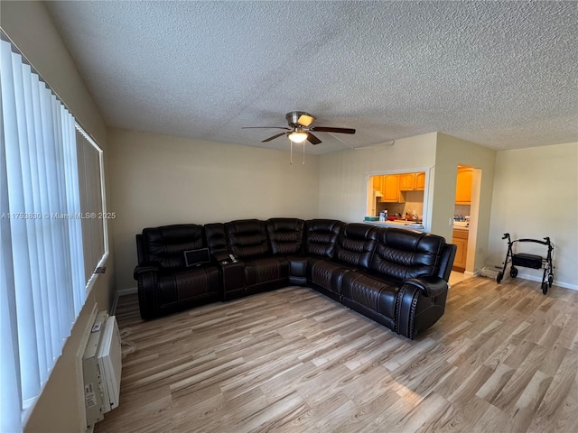 living area with light wood-type flooring, ceiling fan, a textured ceiling, and baseboards