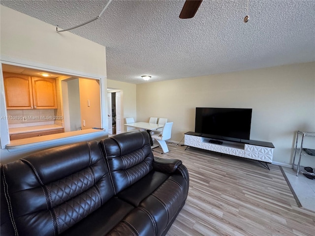 living room featuring a ceiling fan, light wood-style flooring, baseboards, and a textured ceiling