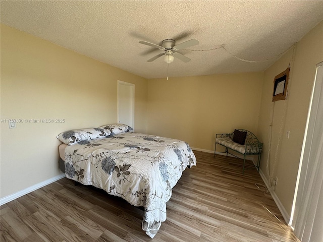 bedroom with a ceiling fan, a textured ceiling, baseboards, and wood finished floors