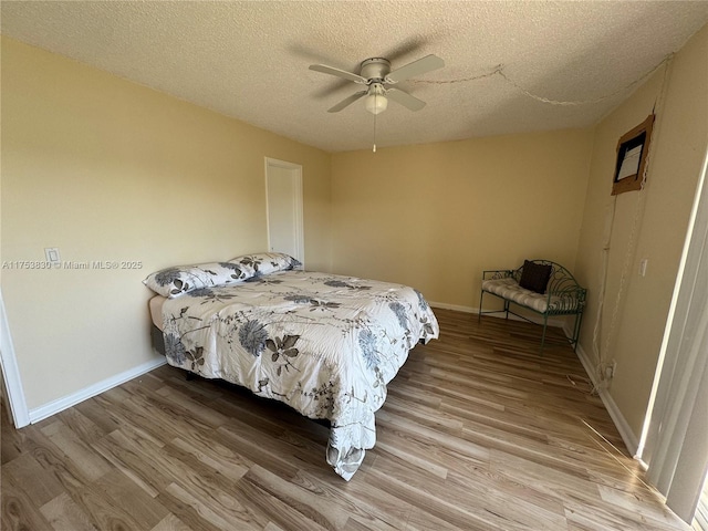 bedroom featuring a ceiling fan, a textured ceiling, baseboards, and wood finished floors