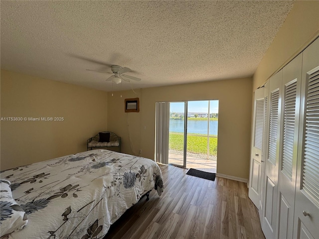 bedroom with a water view, ceiling fan, a textured ceiling, wood finished floors, and access to outside