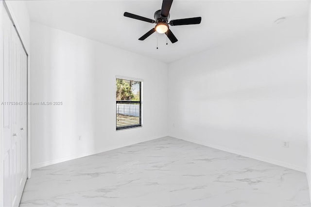 empty room featuring marble finish floor, ceiling fan, and baseboards