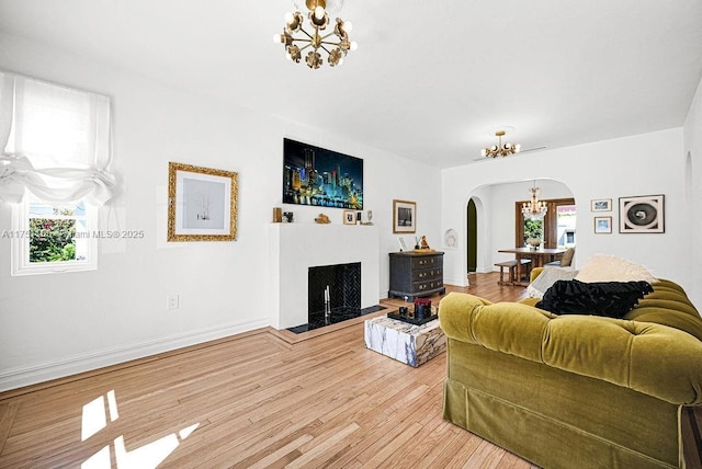 living area with baseboards, arched walkways, light wood-style floors, a fireplace, and a notable chandelier