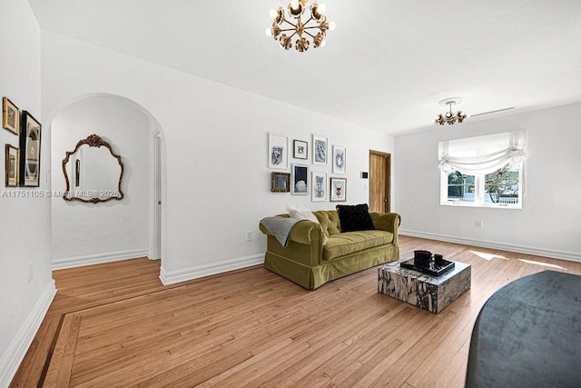 living area featuring arched walkways, baseboards, a notable chandelier, and light wood finished floors