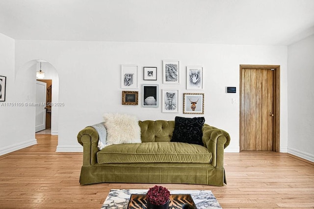 living area with arched walkways, light wood-style flooring, and baseboards