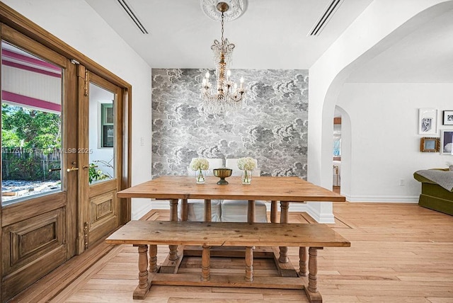 dining room featuring arched walkways, visible vents, light wood-style flooring, a chandelier, and baseboards