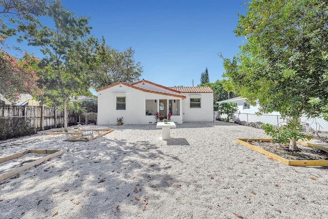 rear view of house with a fenced backyard, a tiled roof, and stucco siding