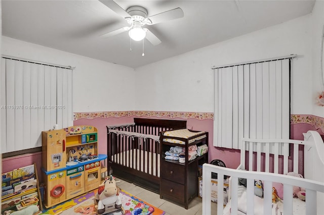 tiled bedroom featuring a nursery area and ceiling fan