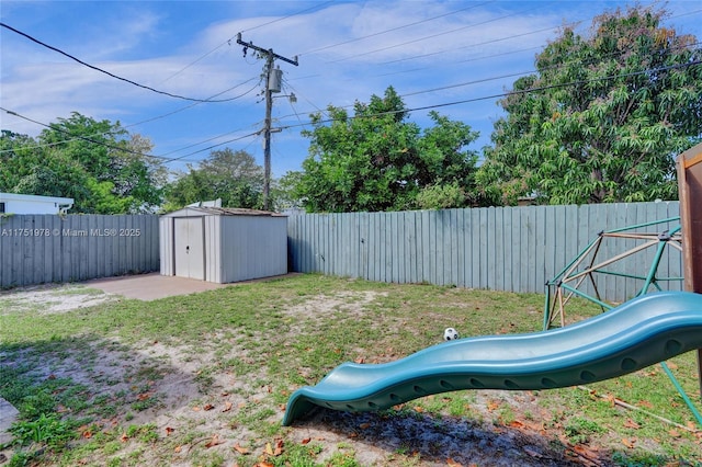 view of yard with a storage shed, a fenced backyard, a playground, and an outbuilding