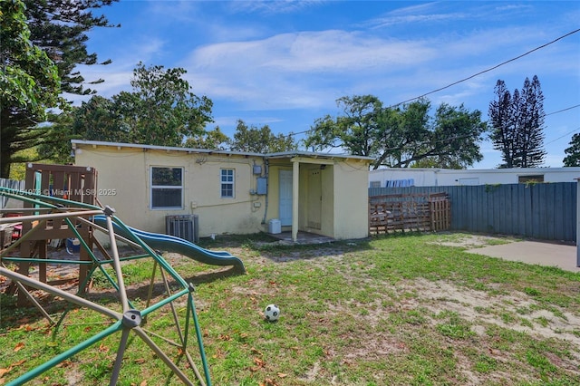 rear view of house with cooling unit, a playground, fence, and stucco siding