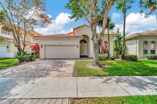 mediterranean / spanish-style house with decorative driveway, stucco siding, a front yard, a garage, and a tiled roof