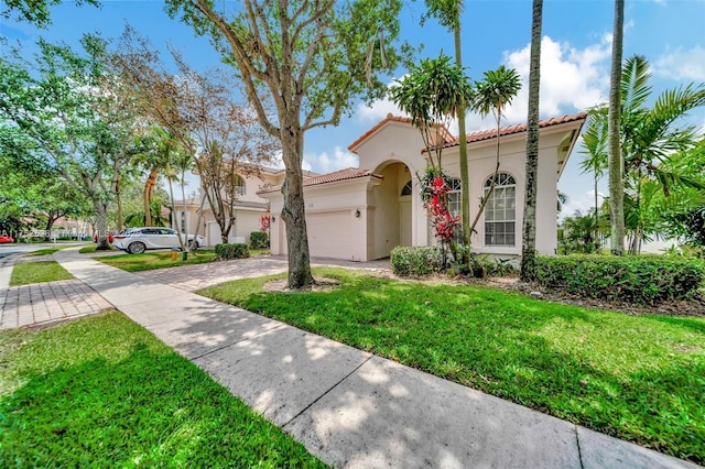 mediterranean / spanish-style house featuring a garage, a tiled roof, decorative driveway, stucco siding, and a front yard