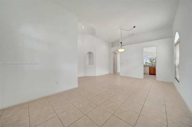 empty room with light tile patterned floors, baseboards, and arched walkways