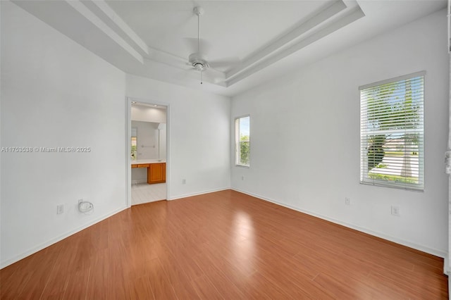 empty room with a ceiling fan, baseboards, a tray ceiling, and wood finished floors