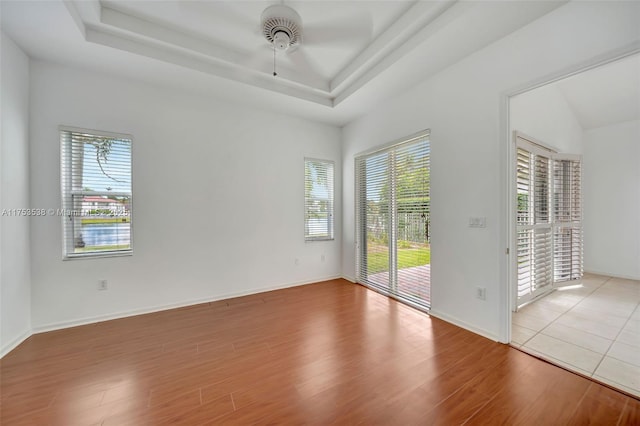 empty room with plenty of natural light, baseboards, a raised ceiling, and wood finished floors