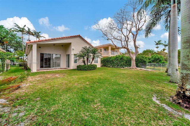 back of property featuring a yard, fence, a tiled roof, and stucco siding