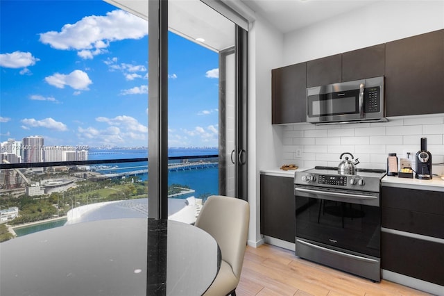 kitchen featuring a city view, stainless steel appliances, light wood-style floors, tasteful backsplash, and a wall of windows