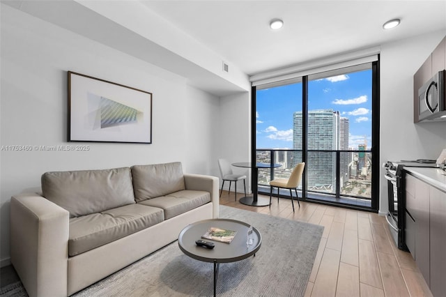 living room with expansive windows, visible vents, light wood-style flooring, and a view of city