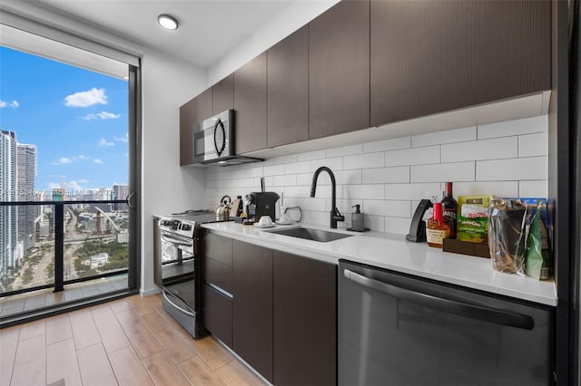 kitchen featuring tasteful backsplash, light countertops, stainless steel appliances, a wall of windows, and a sink