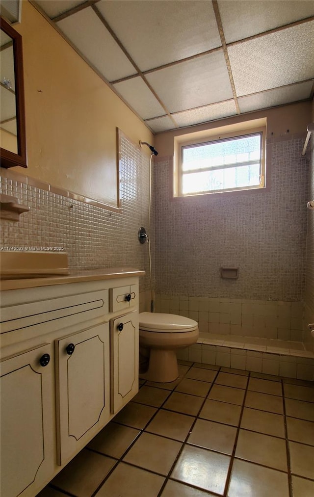 full bathroom featuring tile walls, toilet, a tile shower, vanity, and tile patterned floors